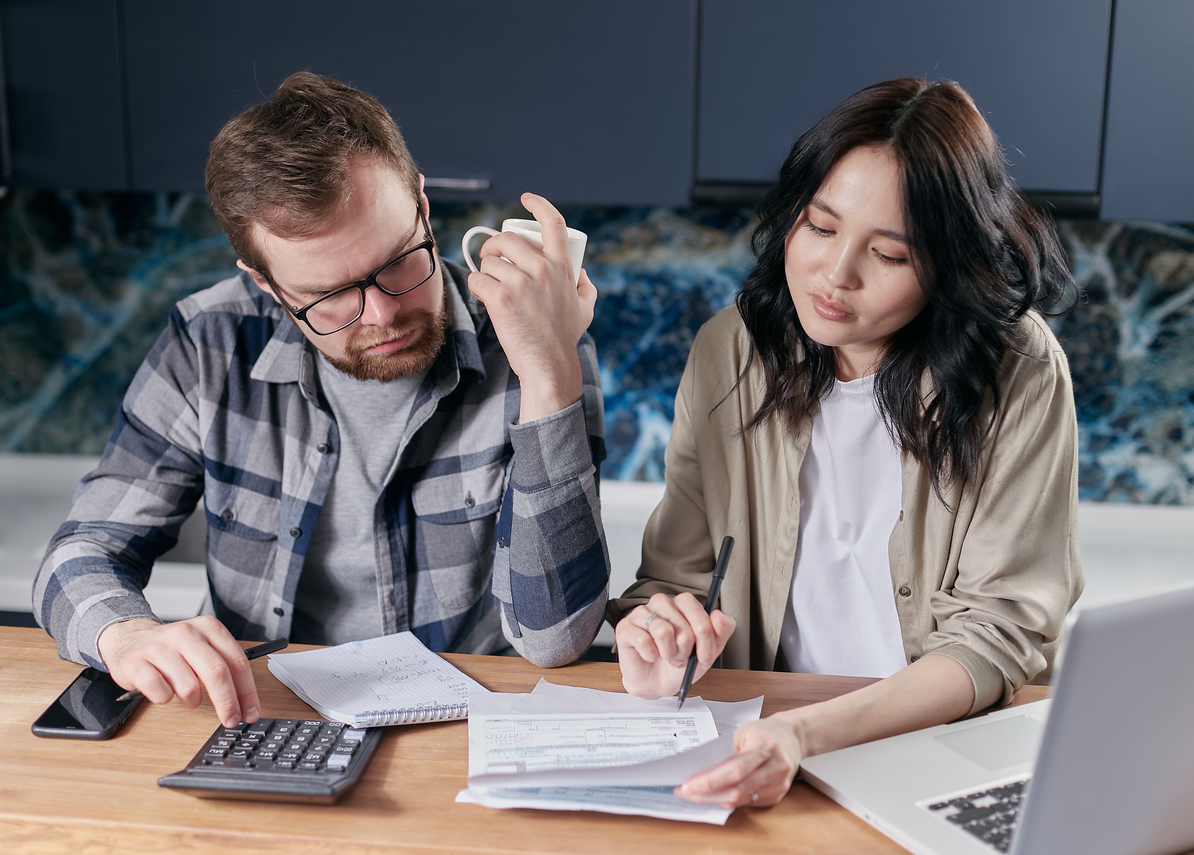 Pareja revisando sus facturas y presupuesto familiar con calculadora y laptop en la mesa de la cocina